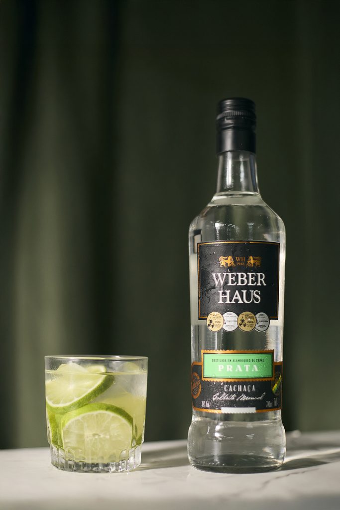 Cachaça Prata Weber Haus ao lado de caipirinha.